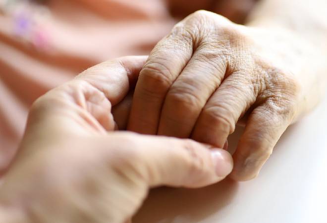 高齢者の手を握る女性の手。